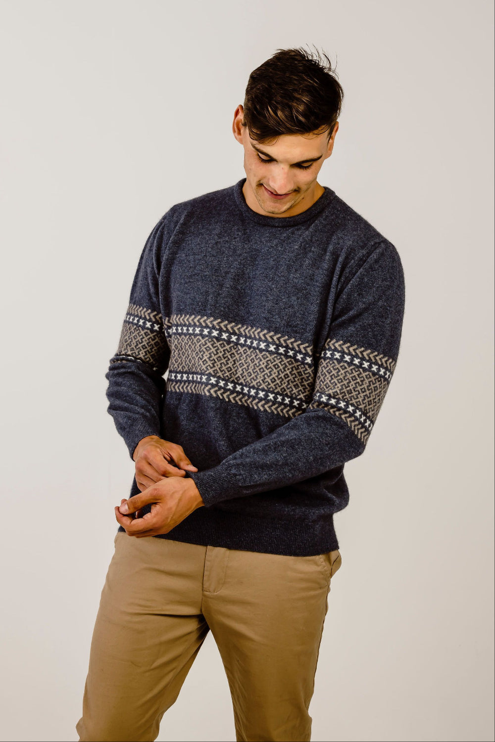 Man wearing a dark blue sweater with a patterned design on a plain background