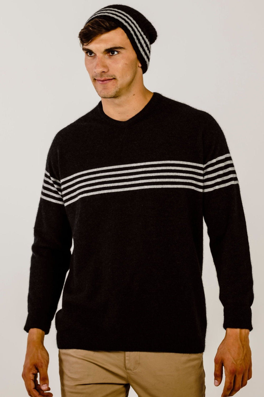 A person wearing a black beanie with grey stripes, standing against a white background.