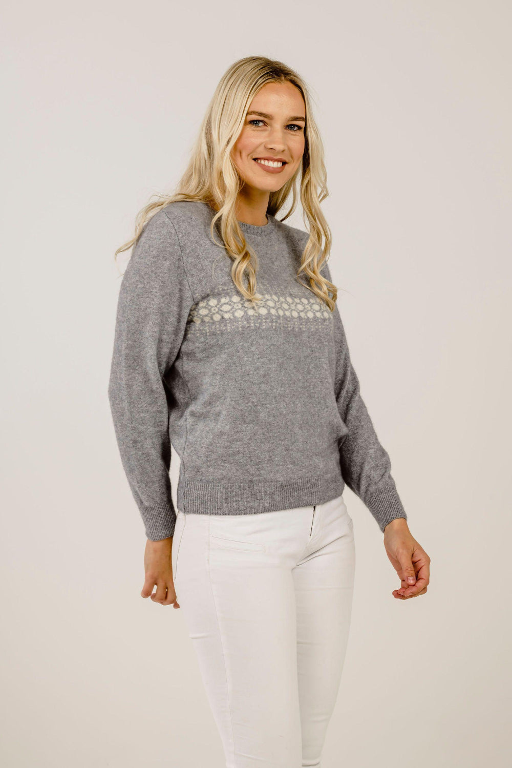 Woman wearing a gray sweater with embellishments on a plain background