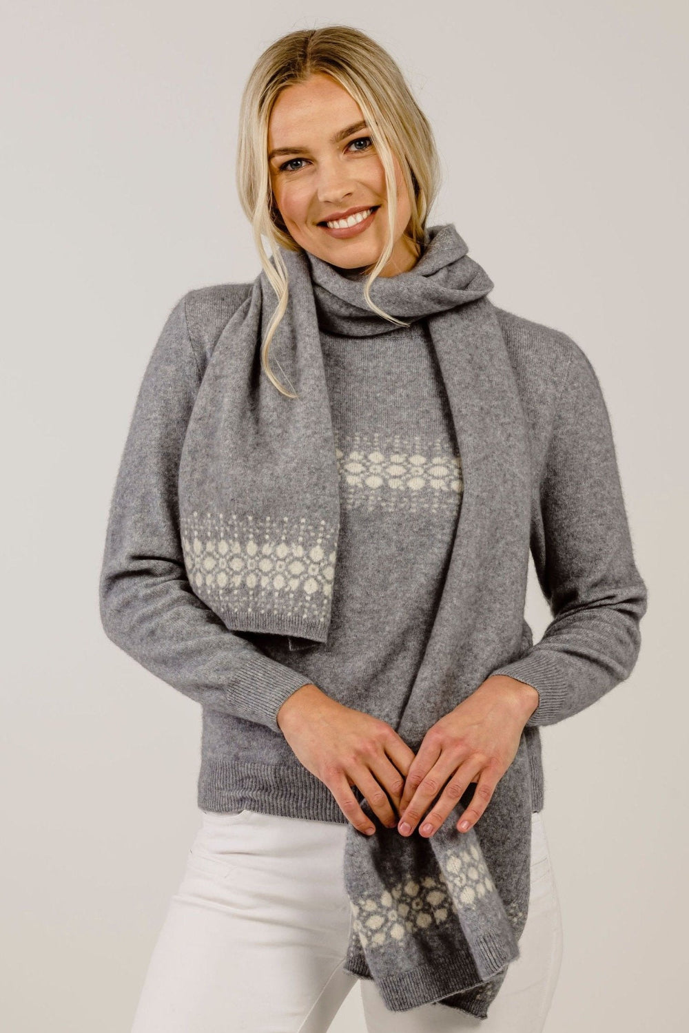 Woman wearing a gray sweater and patterned scarf against a plain background