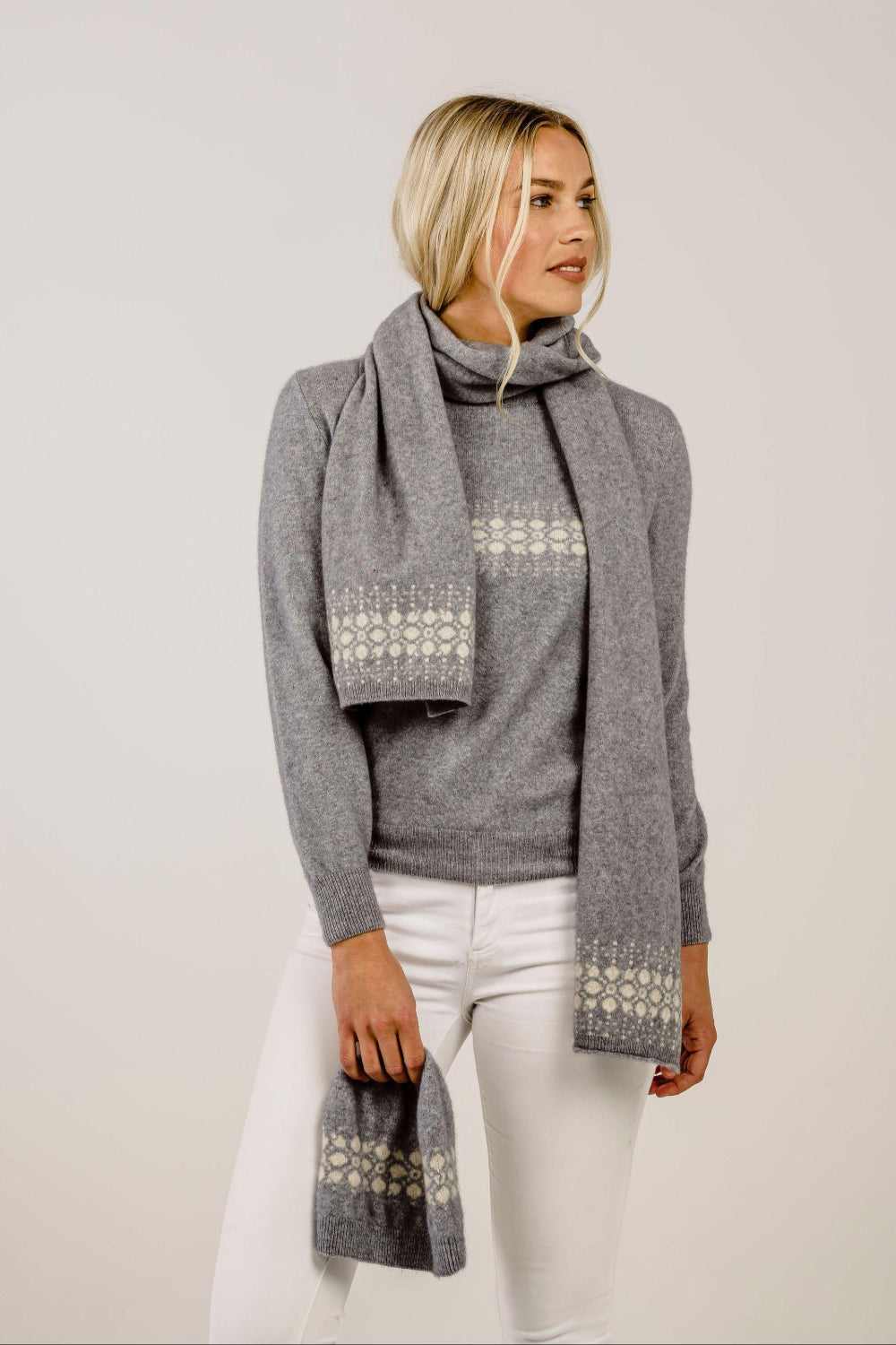 Woman wearing a gray sweater and patterned scarf against a plain background