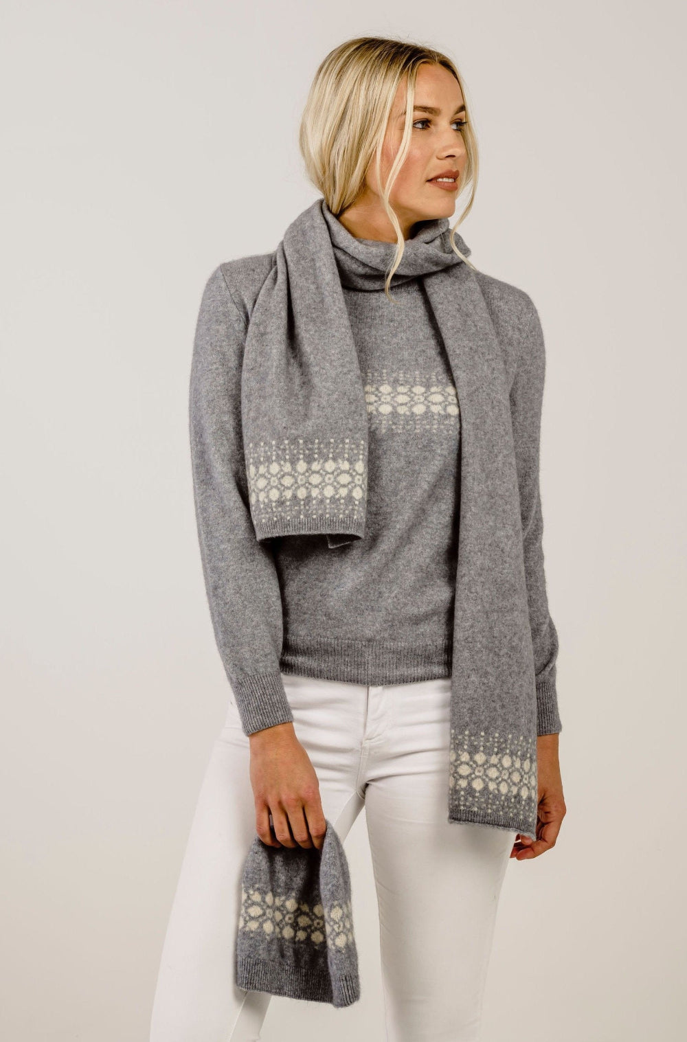 Woman wearing a gray sweater and patterned scarf against a plain background