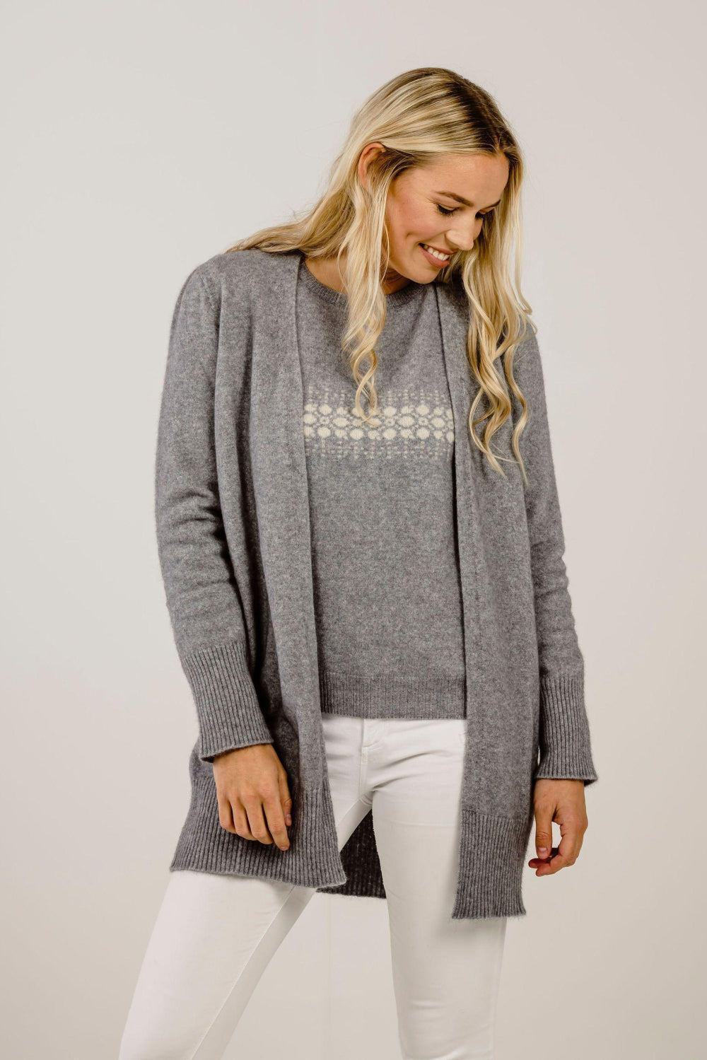 Woman wearing a gray cardigan over a white top with a subtle pattern, standing against a plain background.