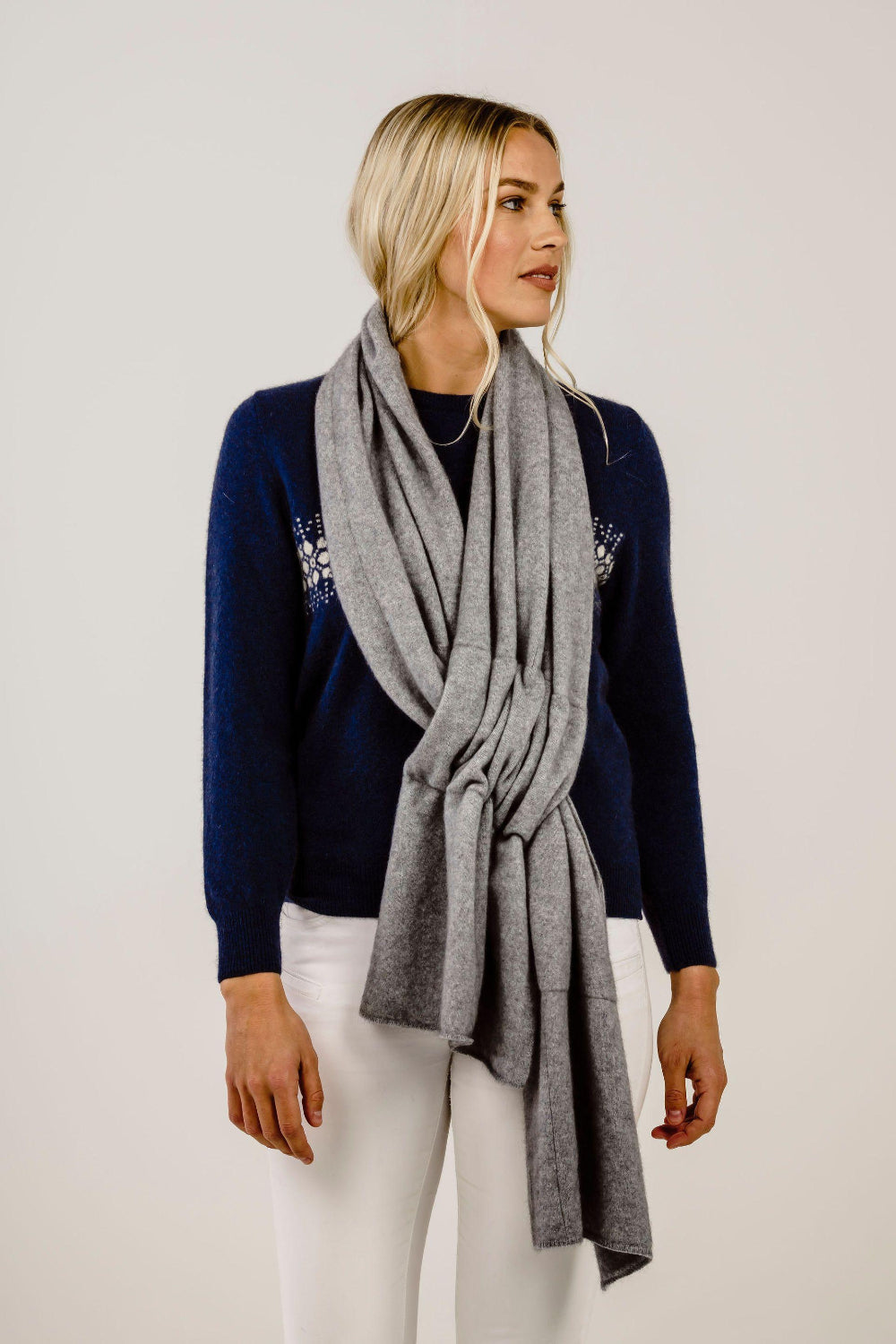 Woman wearing a navy sweater with white pattern and a gray scarf on a plain background