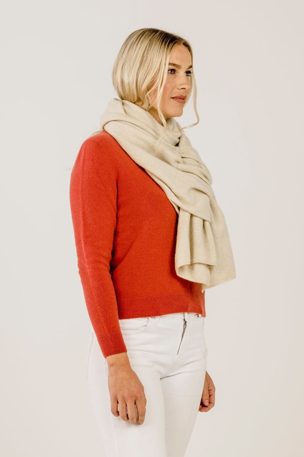 Woman wearing a red sweater and beige scarf on a plain background