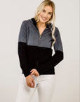 Woman wearing a black and gray color-blocked zip sweater on a plain background