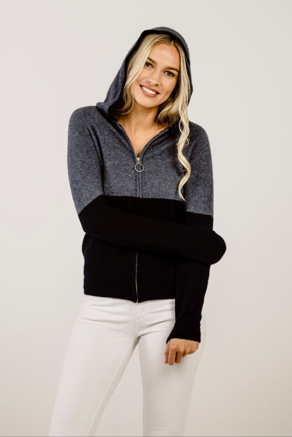 Woman wearing a grey and black  hoodie on a plain background