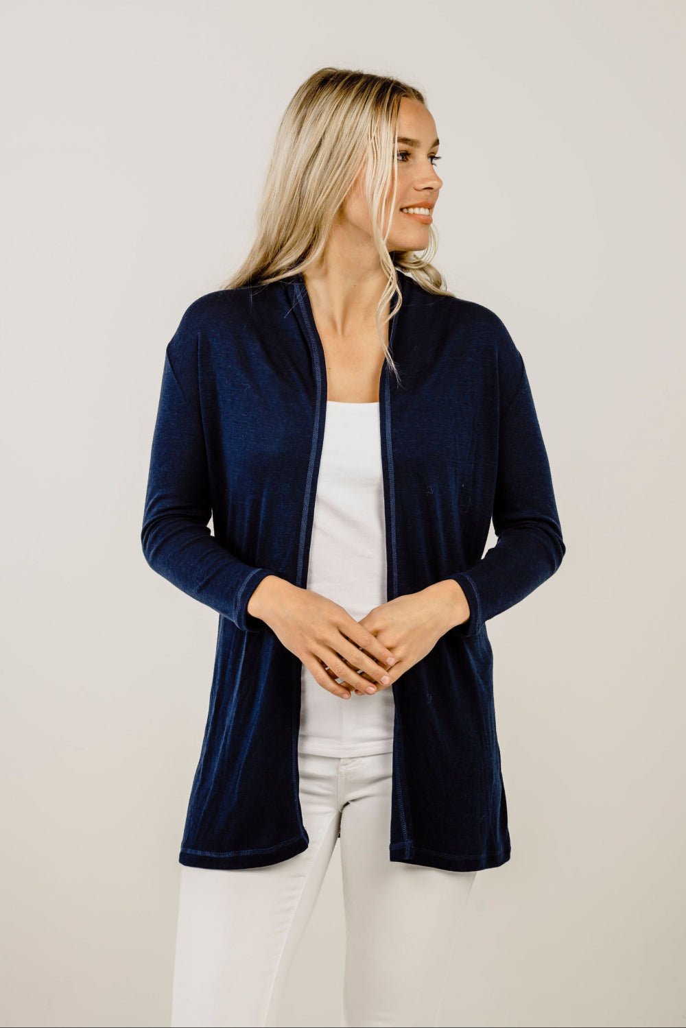 Woman wearing a navy blue cardigan over a white top and pants on a plain background
