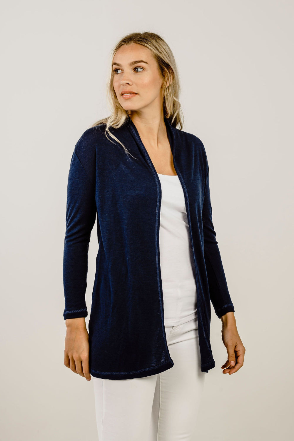 Woman wearing a navy cardigan over a white top and pants on a plain background
