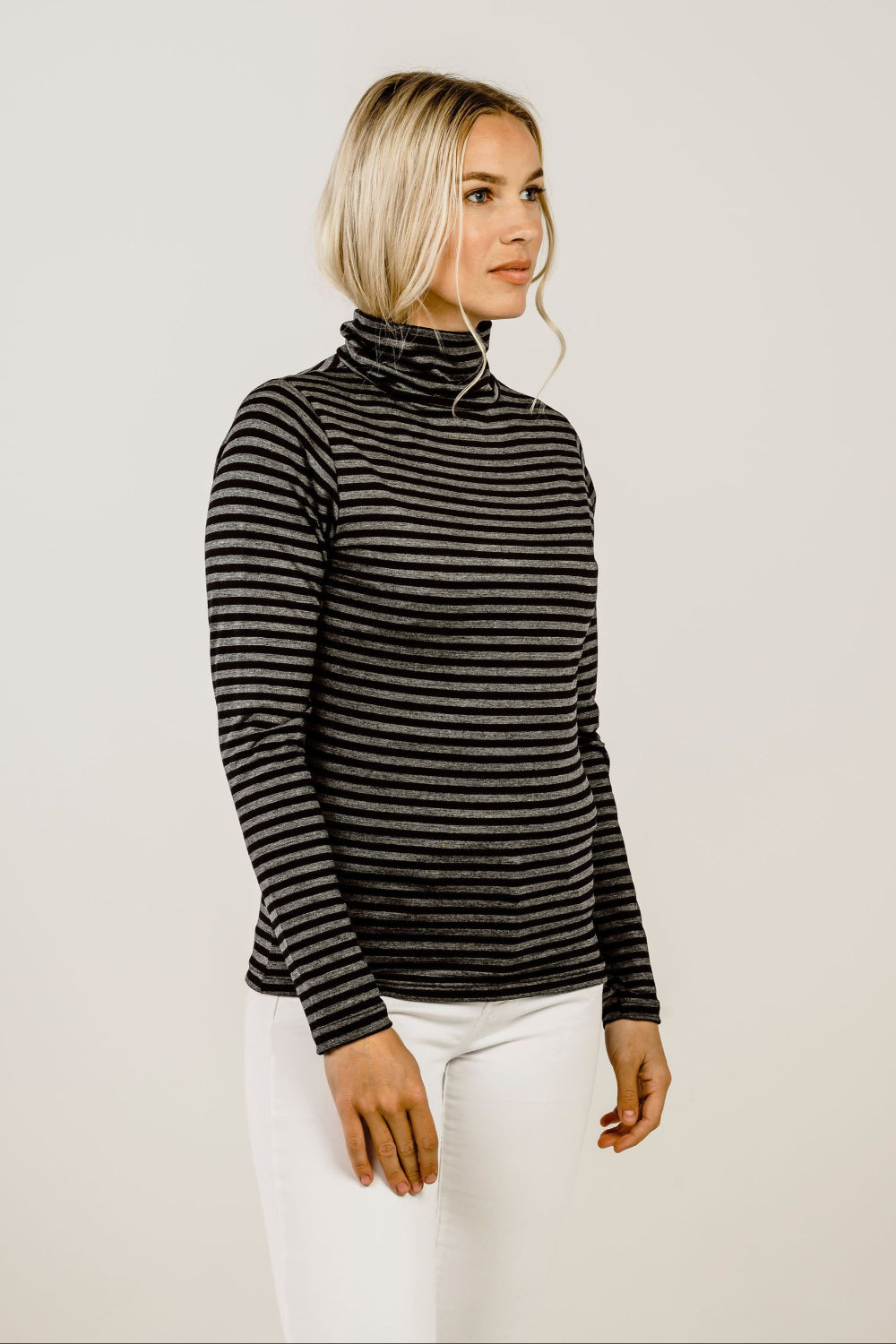 Woman wearing a black and gray striped turtleneck sweater against a plain background