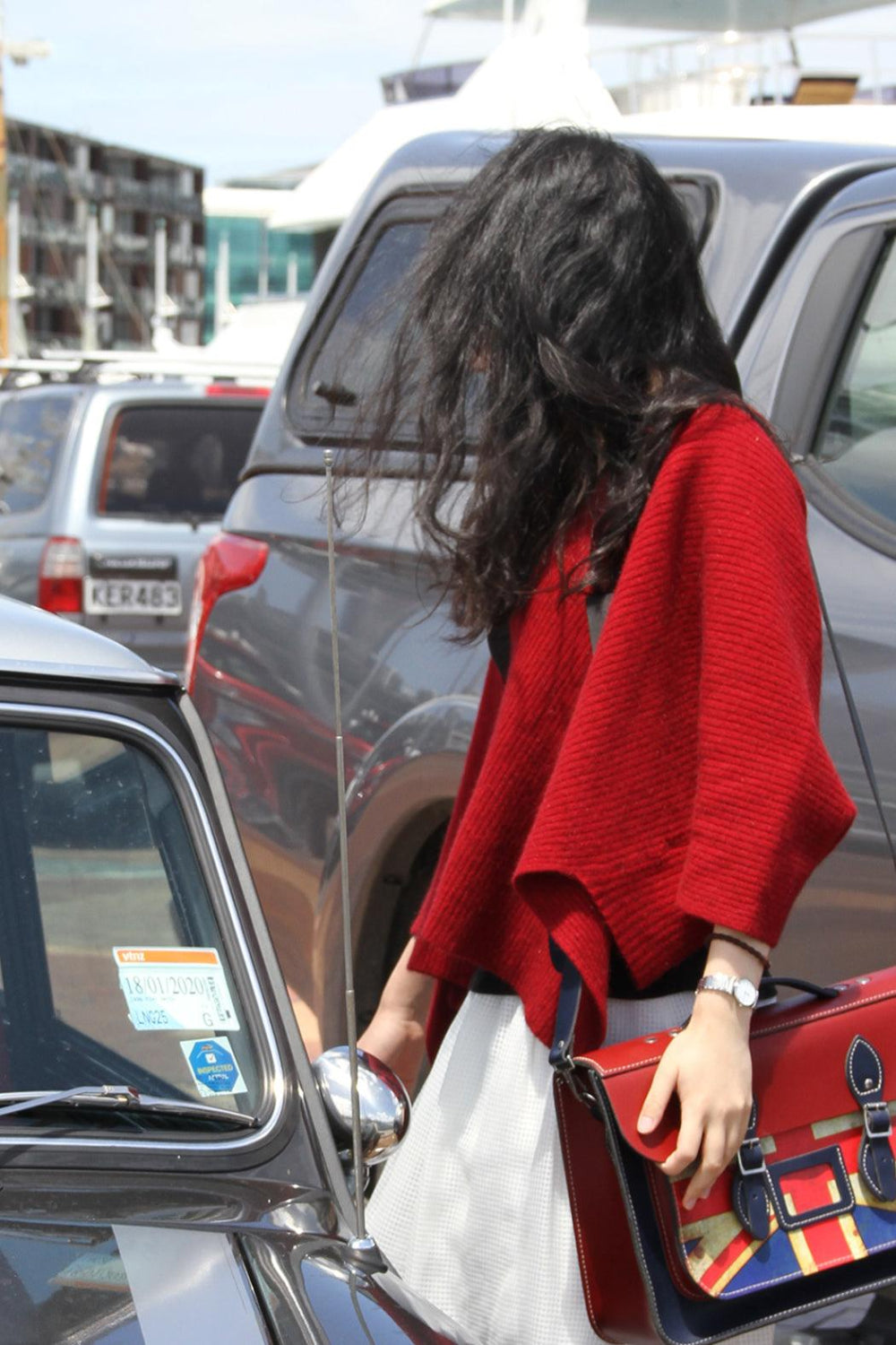 Person in a red sweater standing next to a car with a colorful bag.